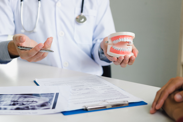 mãos de um(a) dentista com jaleco branco segurando um molde e prótese dentário sob uma mesa de consultório