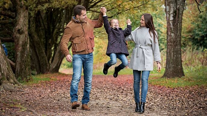 Casal caminhando enquanto levantam a sua filha pelos braços