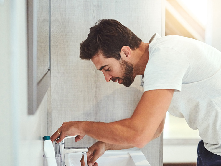 Um homem está lavando sua escova de dentes em um banheiro