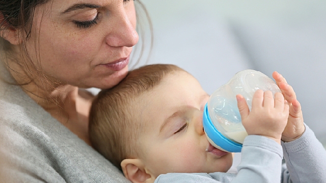 Bebê bebendo biberão no colo da mãe