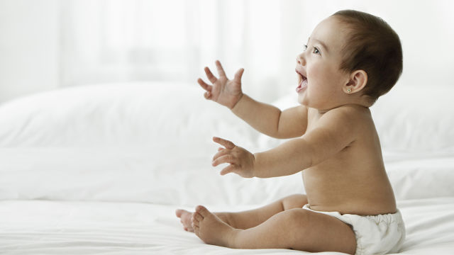 Bebê sorrindo sentado em uma cama