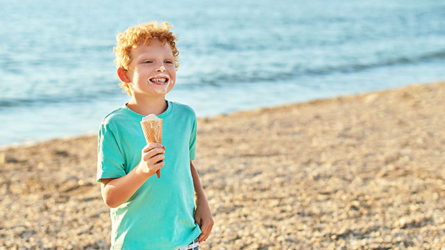 Menino muito feliz comendo sorvete e sorrindo na praia