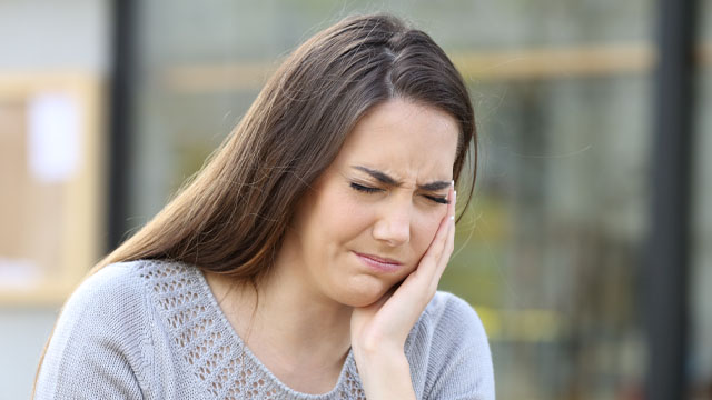 Mulher com a mão na boca sentindo dor de dente ao mastigar