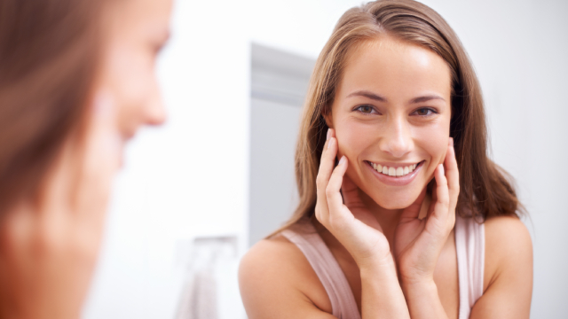 Mulher admirando o esmalte do dente, olhando o seu sorriso no espelho 