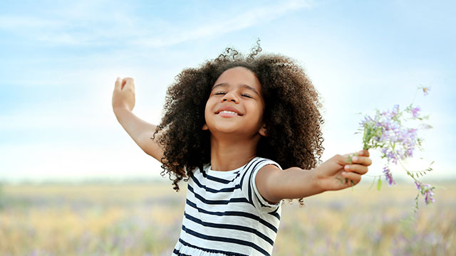 menina sorrindo no campo esticando os braços enquanto segura flores