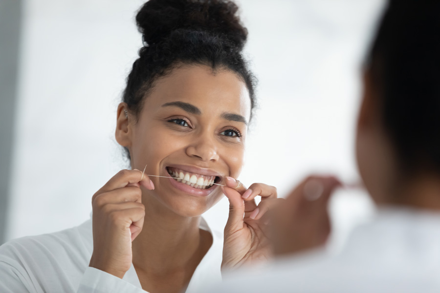 Bela jovem sorridente olhando para o espelho usando o fio dental