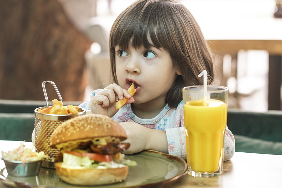 Menina comendo um sanduíche de fast-food com batatas fritas