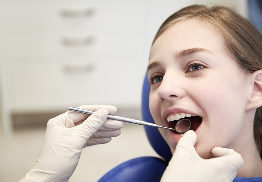 mãos do dentista com espelho dental, verificando os dentes de uma paciente na clínica