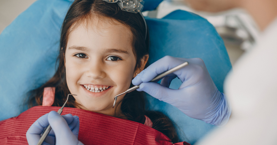 Menina adorável, sorrindo enquanto está sentado em uma Estomatologia Pediátrica