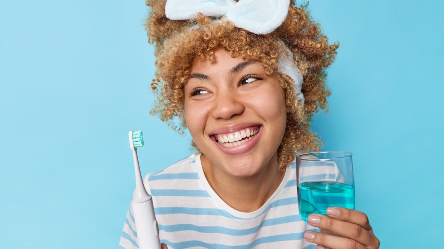 mulher jovem segurando uma escova de dentes e um copo com enxaguante bucal.