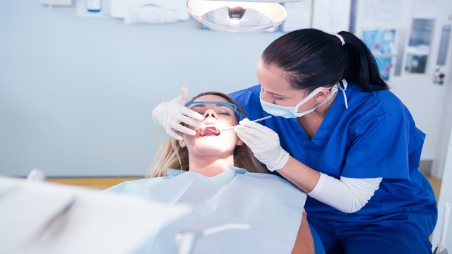 Paciente deitada na cadeira do consultório, sendo examinada pela dentista.