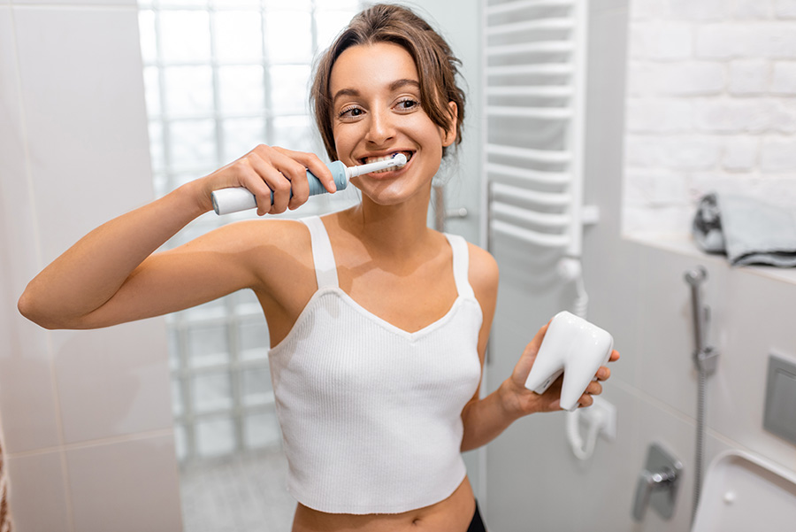 Mulher escovando seus dentes em frente ao espelho com sua escova de dente elétrica recarregável Colgate