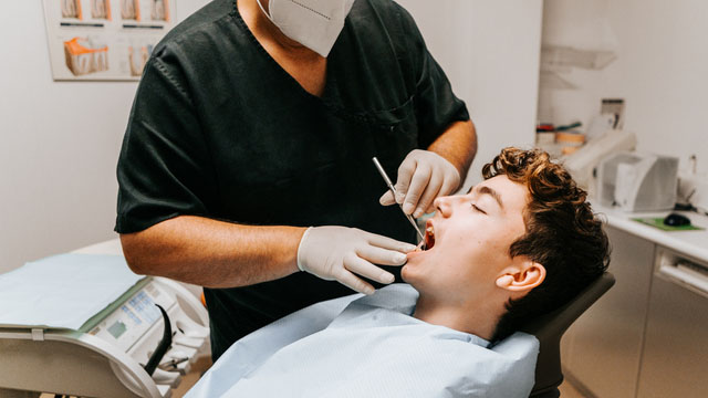 Homem sentado na cadeira do dentista, fazendo raspagem periodontal