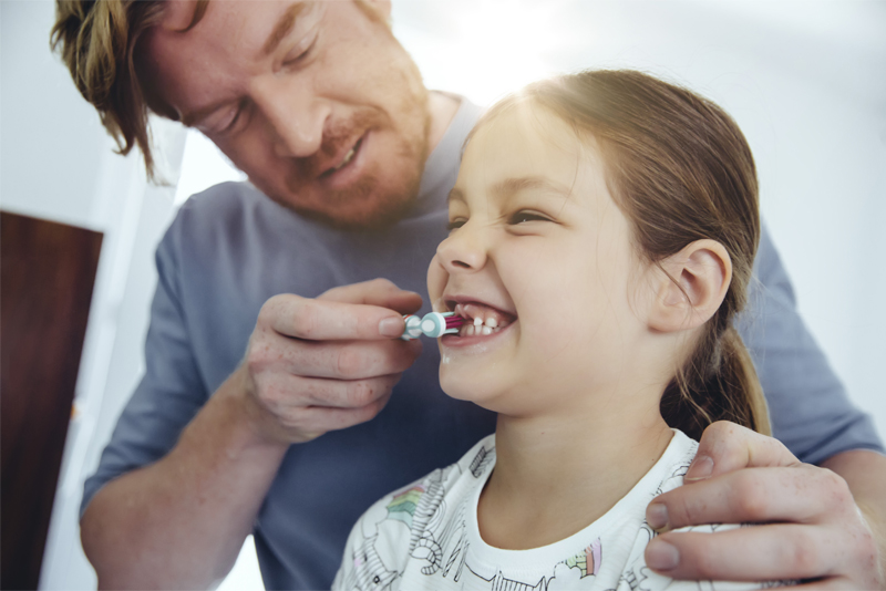 Pai ajudando sua filha a fazer a higiene oral com uma escova de dente infantil