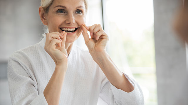 Mulher usando fio dental em frente ao espelho do banheiro